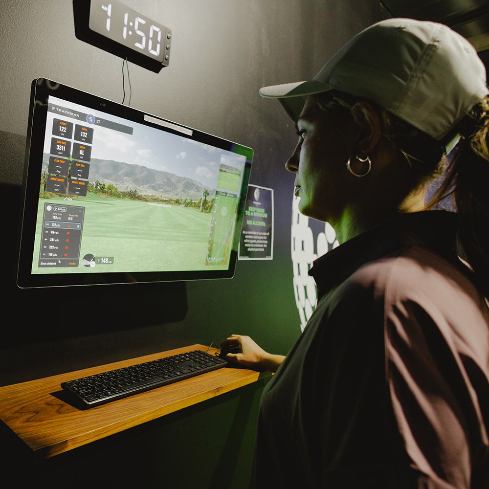 Woman in a hat viewing Trackman golf software on a computer